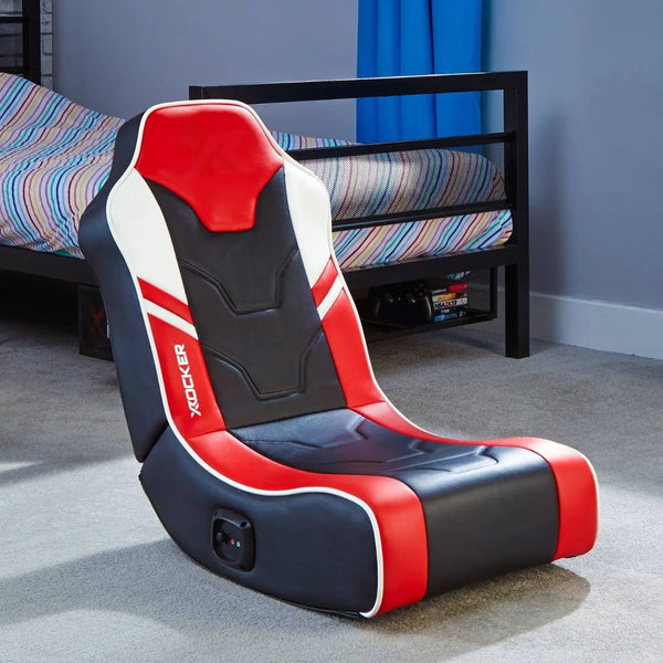 Red and black gaming chair in a room with a bed and colorful bedding.