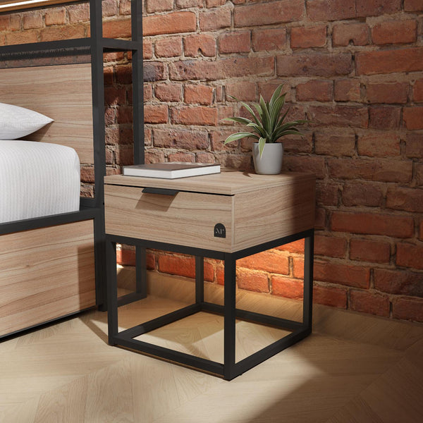 Wooden nightstand with black metal frame next to a bed against a brick wall.
