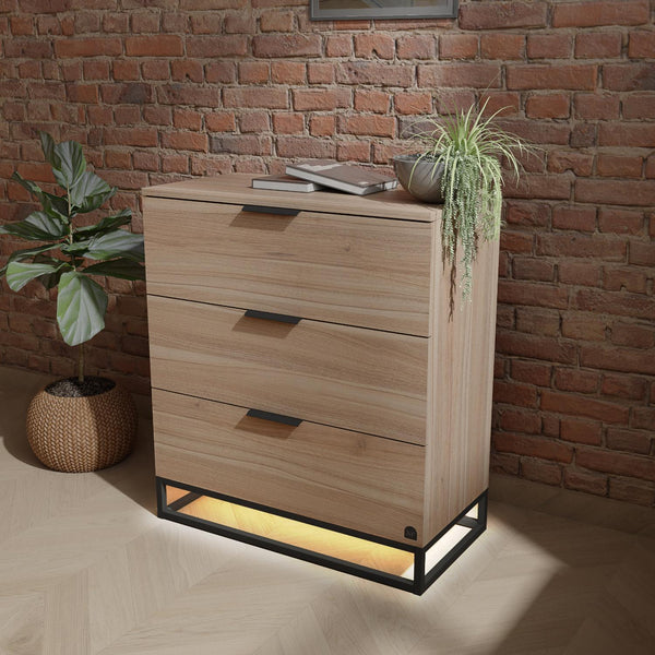 Wooden dresser with three drawers against a brick wall, illuminated from below.
