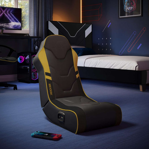 Gaming chair with yellow accents in a bedroom setting with gaming equipment.