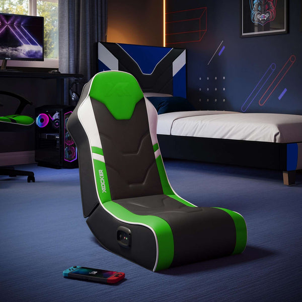 Gaming chair with green accents in a bedroom setting with a bed and TV.