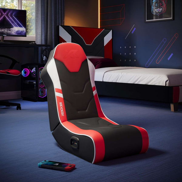 Gaming chair with red and black design in a room with gaming setup and bed.